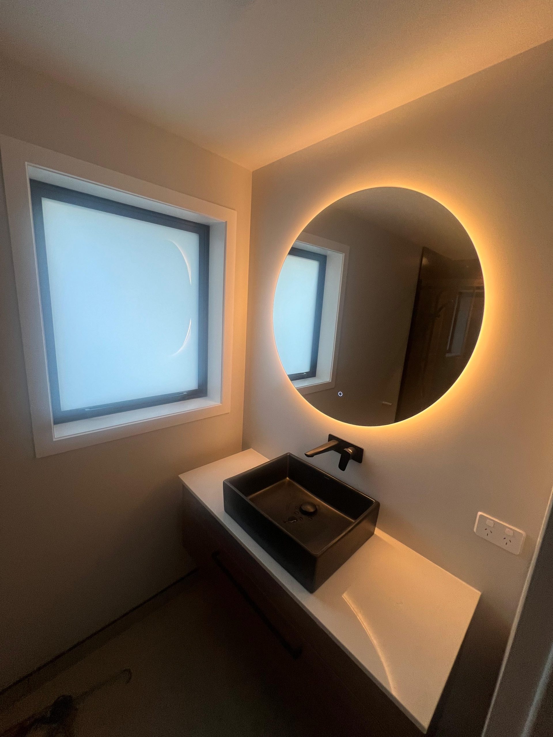 a bathroom with a round mirror and a sink | RNF Construction